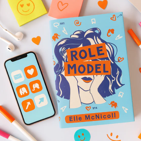 A pastel-themed teenager’s desk with a closed lavender diary covered in cute doodles of rainbows and hearts. Surrounding it are pastel highlighters, jewellery, polaroid photos, a phone, and denim fabric, creating a soft, creative vibe.