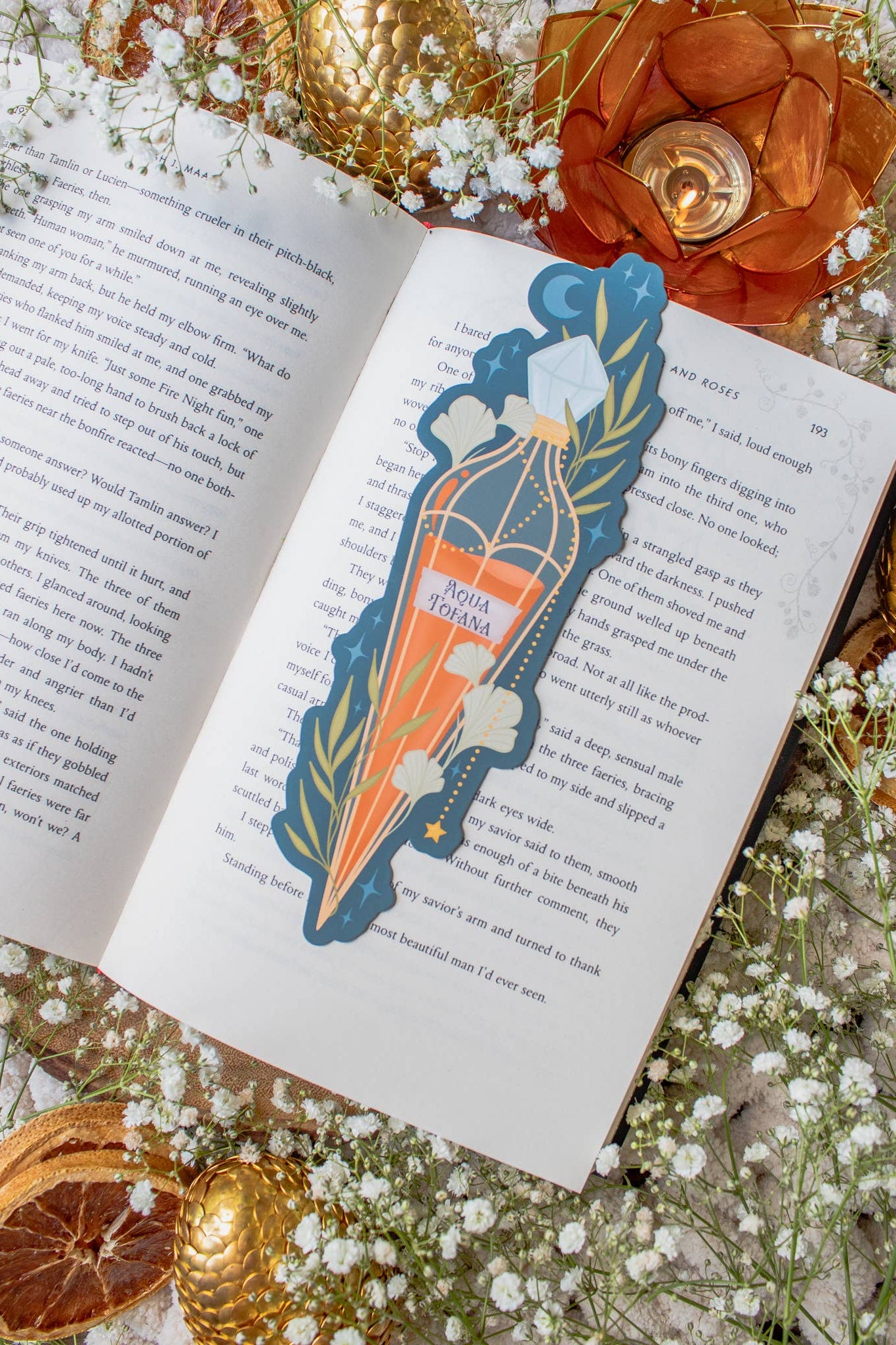 Decorative bookmark with a decorative design on an open book surrounded by flowers and gold elements.