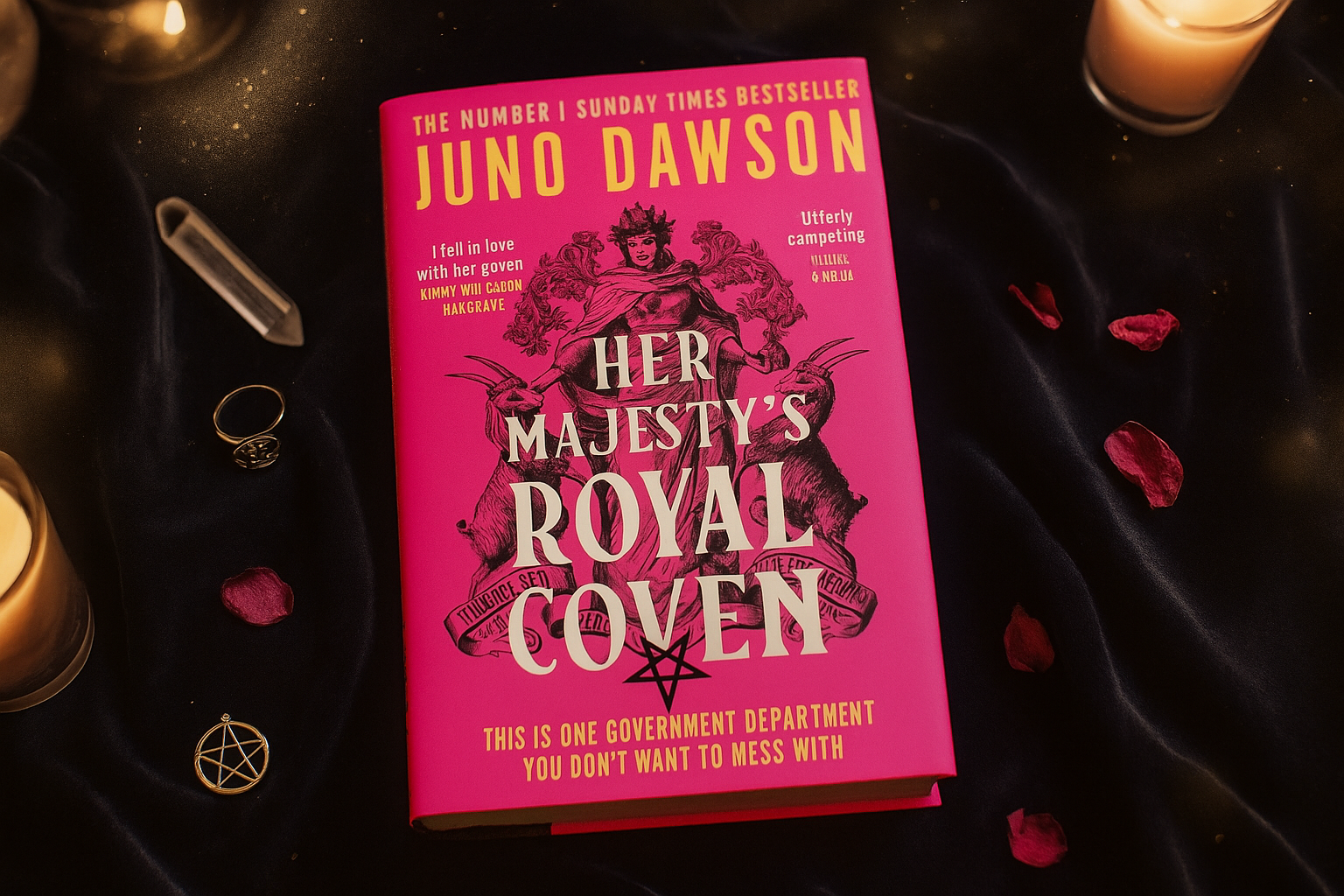 Book titled 'Her Majesty's Royal Coven' by Juno Dawson on a dark fabric background with candles and decorative items.